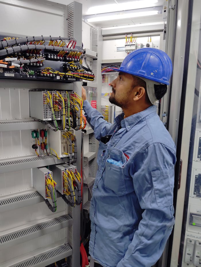 Elektro Rot GmbH Elektriker Elektriker mit blauem Helm überprüft die Verkabelung des Bedienfelds auf Einhaltung der Sicherheitsvorschriften.