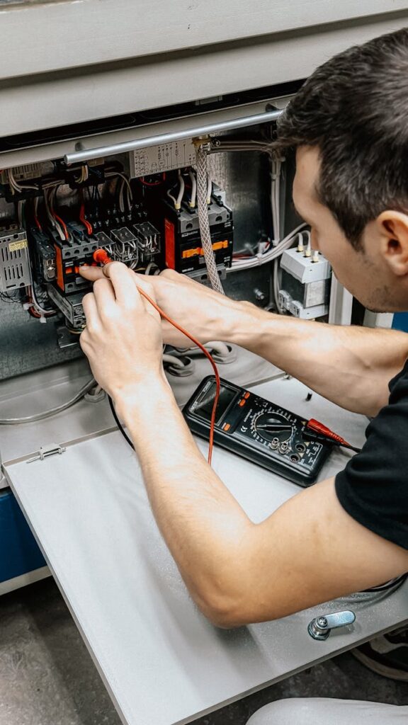 Elektro Rot GmbH Multimeter Ein Elektriker verwendet ein Multimeter, um Verbindungen in einer offenen Schalttafel zu testen und zu diagnostizieren.
